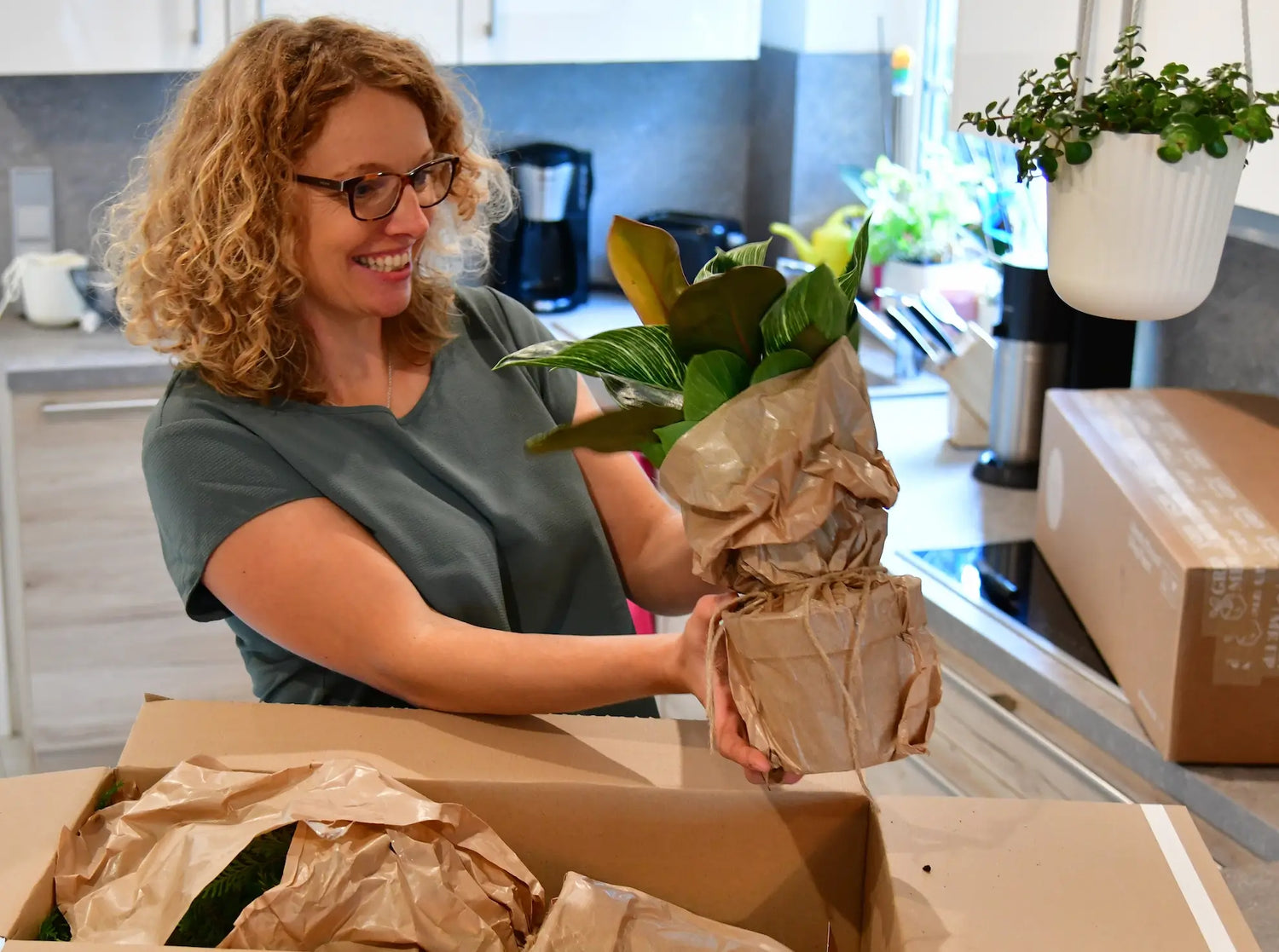 Frau packt glücklich neue Pflanzen in plastikfreier Verpackung in der Küche aus