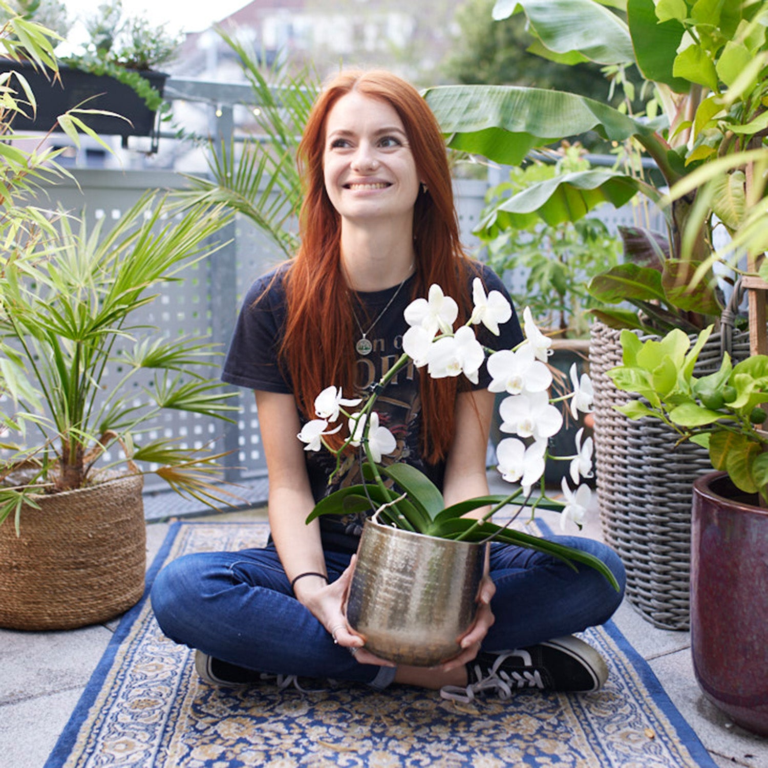 Junge Frau sitzt glücklich mit Orchidee auf dem Balkon