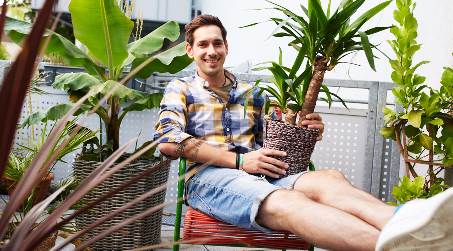 Junger Mann auf Balkon mit Yucca Palme und anderen Grünpflanzen